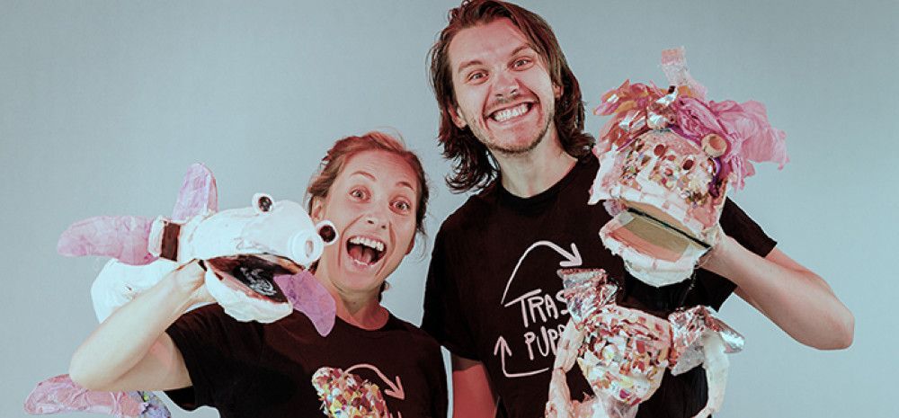 Two individuals behind toy rubbish bins, using cardboard puppets